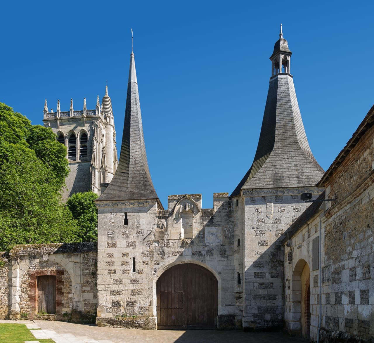 Le portail fortifié de l’abbaye du Bec-Hellouin, ses deux toits d’ardoise en pointe, et la tour Saint-Nicolas derrière.