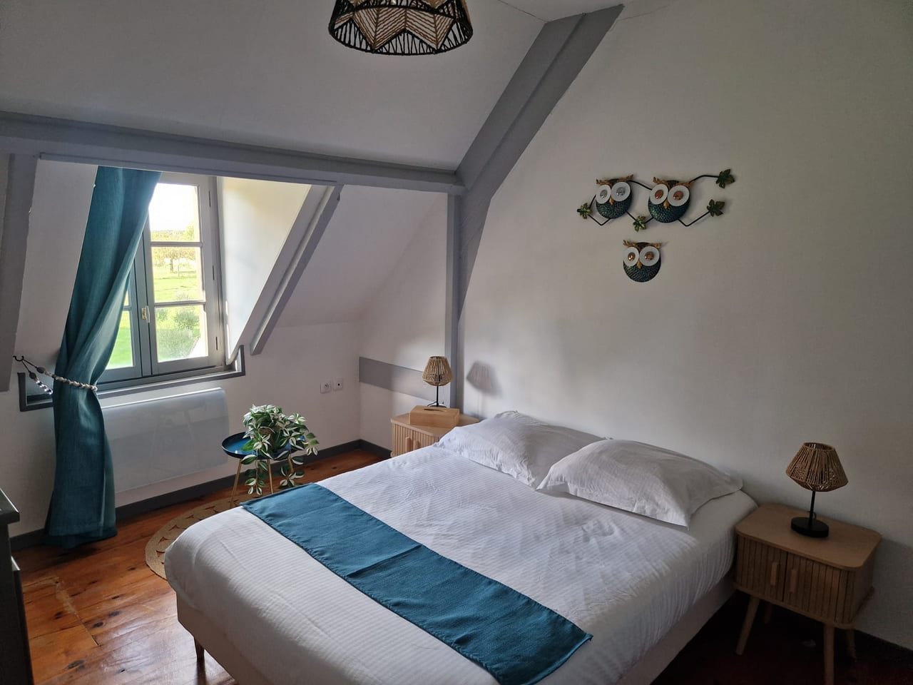 Chambre double sous rampant, rideaux bleu canard et fenêtre ouverte sur le parc