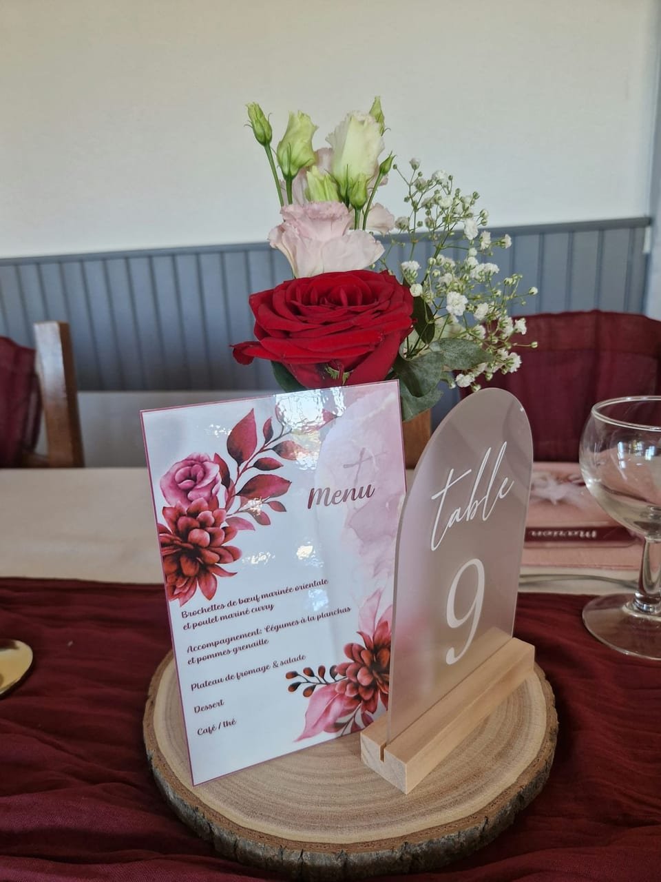 Menu imprimé et numéro de table posés sur un rondin, avec une rose rouge