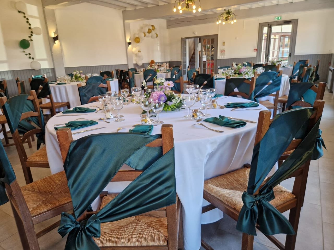 Tables rondes nappées de blanc, nœuds de chaise vert sapin et centres de table champêtres